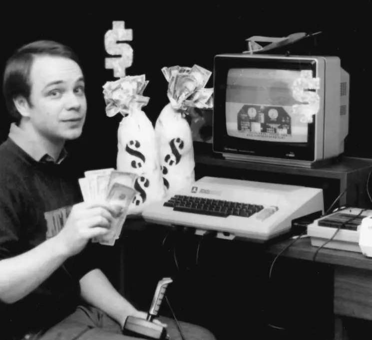 Sid Meier in a recruiting ad holding money in front of a computer to entice new developers to join MicroProse